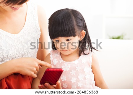 mother and little girl using smart phone together on sofa