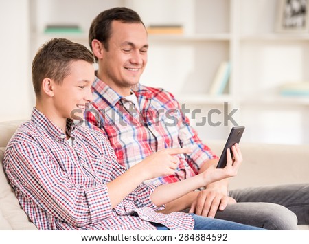 Boy sitting at sofa at home with father and using laptop.