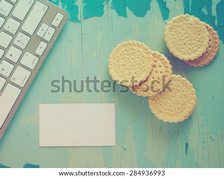 Computer keyboard, biscuits and empty business card on blue painted weathering table. Grunge style