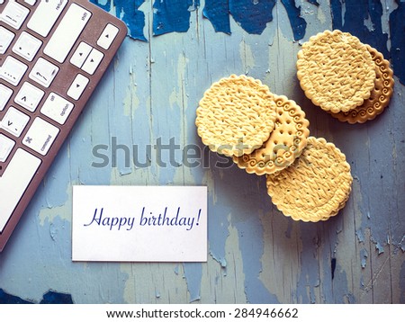 Computer keyboard, biscuits and business card with iscriptions "Happy birthday!" on blue painted weathering table. Grunge style