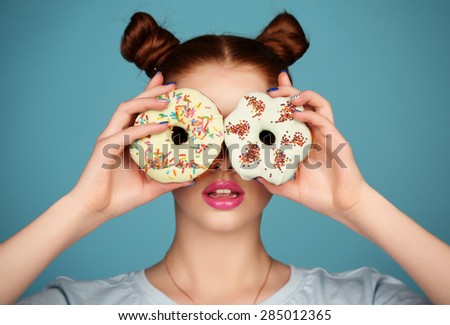 fashion studio photo of beautiful young girl with dark hair and bright makeup holding sweet donuts 