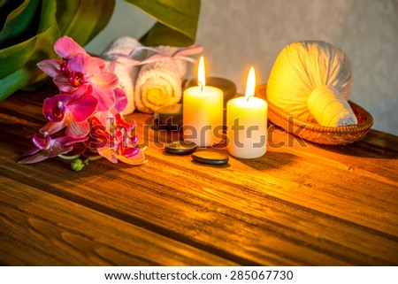 spa concept of pink orchid flower, thai herbal compress balls in basket, towels, zen stones and candles on wooden background