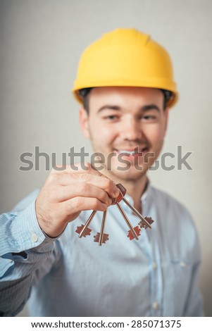 The man in yellow helmet holding keys. On a gray background.
