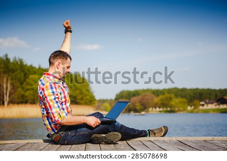 Excited young man using laptop near the lake