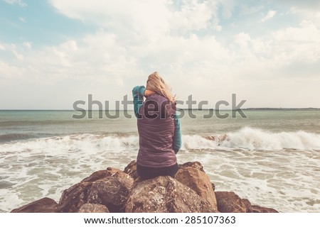 Young woman sitting on stones on the sea coast.