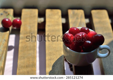 Ripe red cherry in a cup on a wooden surface