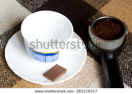 Empty cup, peace of chocolate and coffee machine horn on a checkered English plaid
