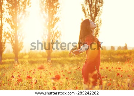 Young woman enjoying nature and sunlight in poppy field