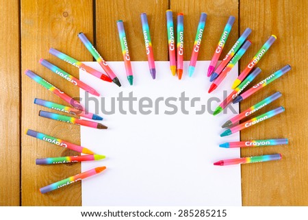 Colorful pastel crayons with white sheet of paper on wooden table, top view