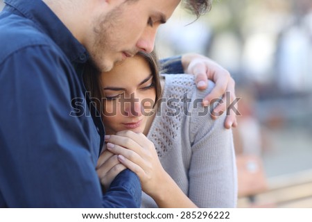 Man comforting his sad mourning friend embracing her in a park Royalty-Free Stock Photo #285296222