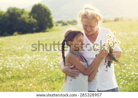 Great-grandmother and granddaughter standing in flower field in sunlight Royalty-Free Stock Photo #285328907