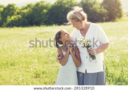 Great-grandmother and granddaughter standing in flower field in sunlight Royalty-Free Stock Photo #285328910