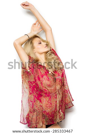Beautiful blond girl with long hair in red silk summer tunic and bikini bottom posing over white wall.