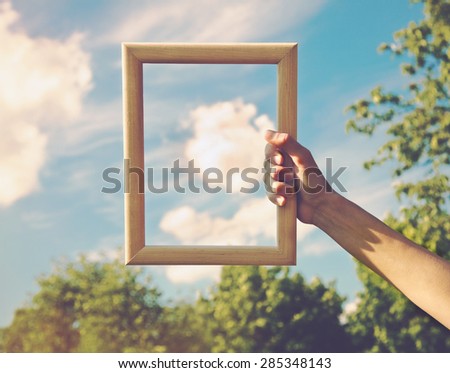 Hand holding a wooden frame on cloud background. Care, safety, memory or painting concept.