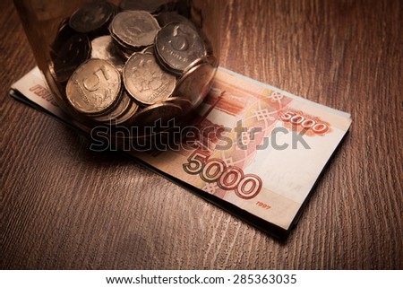 Bundle of bank notes and a glass jar with coins on a wood background