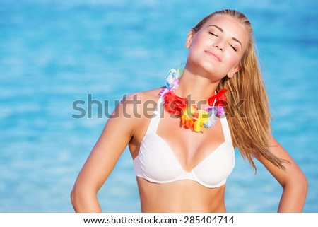 Portrait of beautiful happy woman on the beach, enjoying bright sunny day with closed eyes, wearing traditional Hawaiian necklace of flowers, active summer vacation
