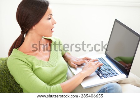 Waist up portrait of a young woman looking surprised at her laptop screen