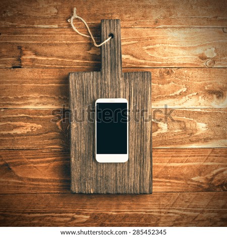 Top view of smart phone on vintage cutting block on wooden background. Toned photo