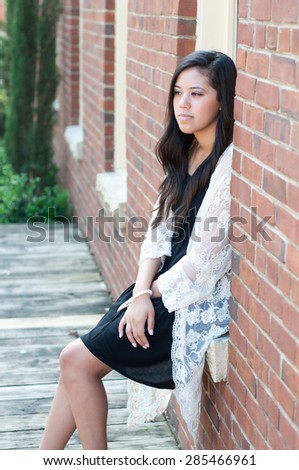 Outdoor shot of attractive teen wearing a dress and sitting in window of brick building.