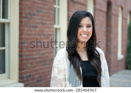 Beautiful and happy senior graduate standing in front of building wearing a dress.