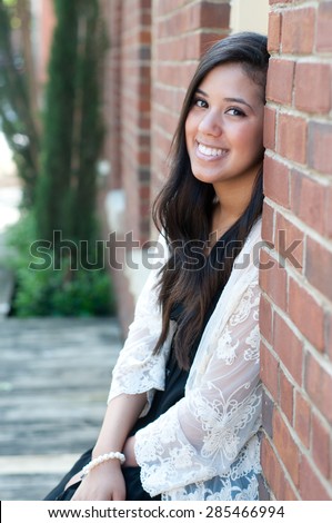 Outdoor shot of beautiful teen with a big smile, sitting in window of brick building.