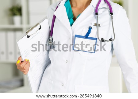Female medicine doctors holding clipped document pad with badge on her chest closeup. Medical help or insurance concept. Doctor is waiting for patient to examine. Physician reception concept