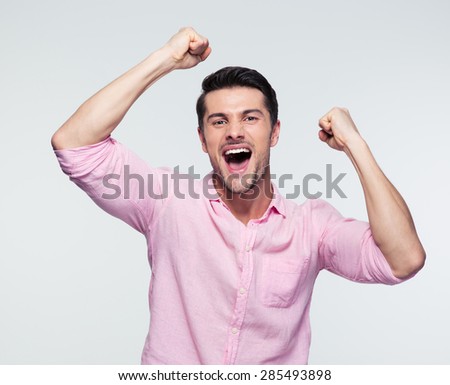 Cheerful handsome young businessman celebrating his success over gray background. Looking at camera