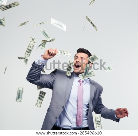 Businessman standing under money rain over gray background