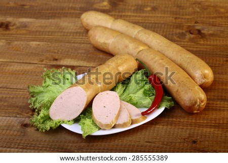 Meat home made sausages green fresh lattuce and red pepper on plate on wooden table top, horizontal picture