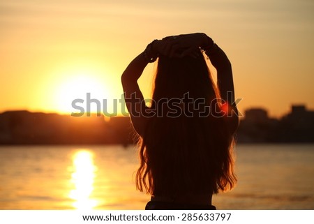 Beautiful and fashion young woman in boho fashion style outfit posing at beach. Slim girl standing and looking to a sea. Female silhouette in the sunset on the beach. Vitality healthy living concept