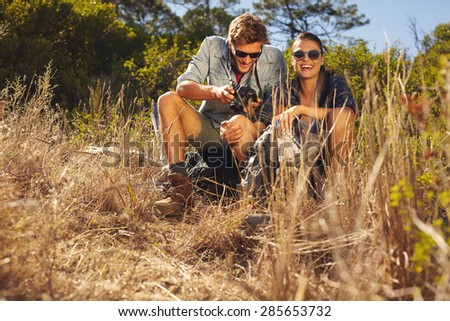 Outdoor shot of young couple on hiking trip taking a break. Woman smiling while man looking at his camera.