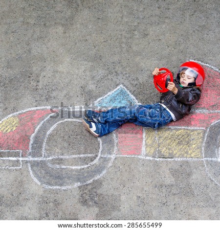 Funny kid boy having fun with race car picture drawing with colorful chalks. Creative leisure for children outdoors in summer