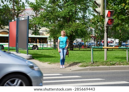 Young woman stands at a traffic light and waiting for green signal