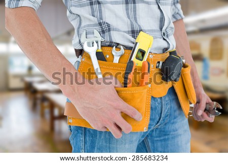 Cropped image of technician with tool belt around waist against workshop