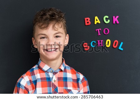 Back to school concept. Portrait of a schoolboy at the black chalkboard.