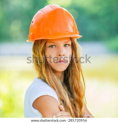 Portrait of beautiful teenage girl in an orange helmet, against green of summer park.