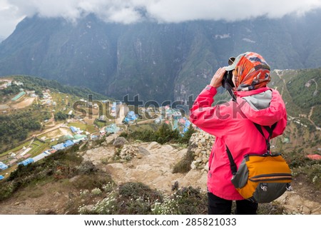 Young female photographer  tourist standing above mountain village taking pictures buildings, Namche Bazaar, Nepal.