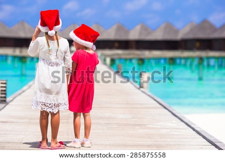 Little adorable girls in Santa hats during beach vacation at wooden jetty