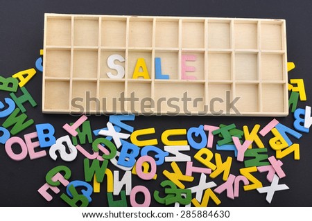 Spilling Colorful Alphabets on Black Background with "SALE" Word on Wooden Block, Selective Focus