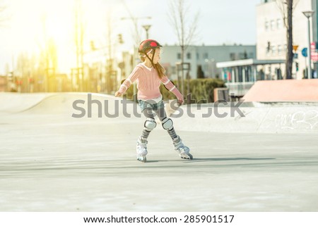Little pretty girl on roller skates in helmet at a park
