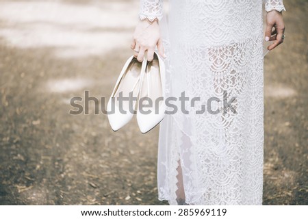 Beautiful bride in a white dress holds her shoes and stands on the ground with her bare feet
