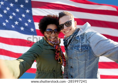 people, international friendship and technology concept - happy international teenage couple taking selfie over american flag background