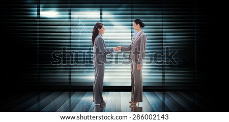 Businesswomen shaking hands against room with large window looking on city