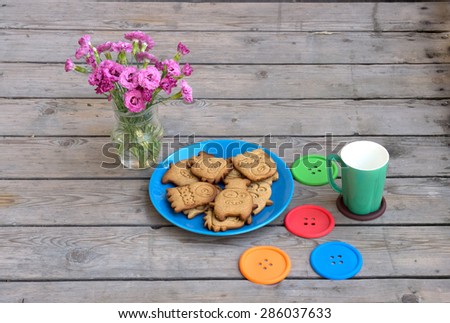 Cookies monsters on a blue plate with a vase of flowers and stand under coffee.