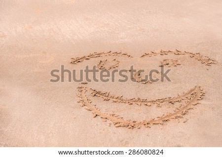Handwrite face on the sand at the beach.