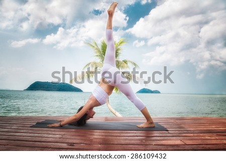 Young woman doing yoga asana at pier of tourist resort