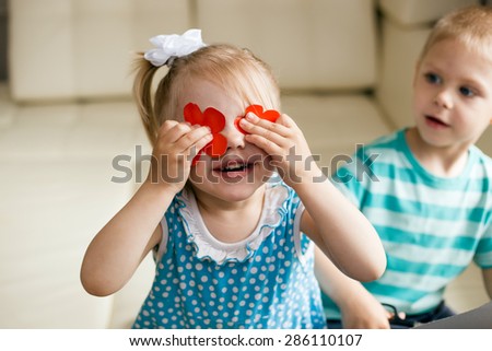 the girl closed her eyes red paper cut outs flowers standing next to the boy and stares at the baby