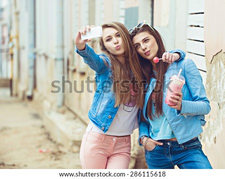 Hipster girlfriends taking a self photo in urban city background