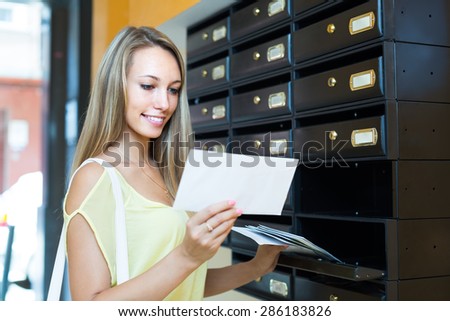 Smiling girl taking junk mail out the posting box Royalty-Free Stock Photo #286183826