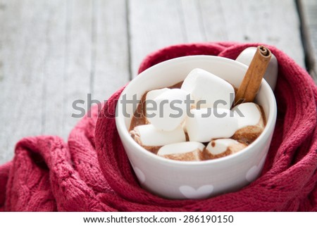 Hot chocolate in grey heart cup with marshmallow and cinnamon, knitted scarf, rustic wood background